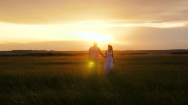 Gün batımında bir kadınla bir erkeğin silueti. Romantik randevu ve doğada aşk. Güzel bir kız ve bir adam yeşil çimlerin üzerinde el ele yürüyorlar. Aşık genç bir çift seyahat ediyor..