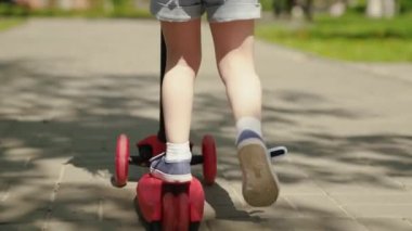 Küçük bir kız scooter sürmeyi öğreniyor. Aile hafta sonu dışarıda. Mutlu çocuk parkta oynuyor. Sağlıklı bir çocuk şehirde scooter kullanıyor. Mutlu bir çocukluk, aile, sağlık kavramı..