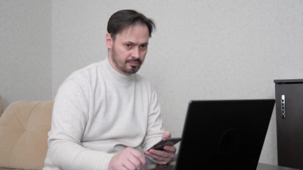 Biznesmen, pracujący na laptopie, mówiący przez smartfona. Mężczyzna pracuje na komputerze i komórce w biurze, w domu. Wolny strzelec pracujący z nowoczesnym laptopem. — Wideo stockowe
