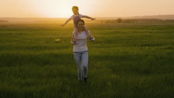 Anya és lánya a mezőn játszanak naplementekor. Boldog család. Anya a gyerekkel, a lánya a repülésről álmodik, a család a zöld fűben fut a napsütésben. Boldog család és összetartás. Hétvége a természetben — Stock videók
