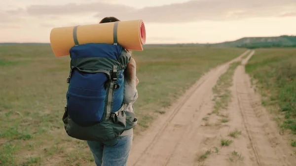 Giovane escursionista donna escursioni in montagna in estate. Donna caucasica sana attiva con zaino sta camminando verso una montagna lontana. Viaggiatore viaggia su una strada di campagna, meditazione, bioturismo, escursioni. — Foto Stock