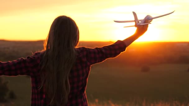 Free Girl chce zostać pilotem i astronautą. Zwolnij trochę. Szczęśliwa dziewczyna biegnie z zabawkowym samolotem na polu w świetle zachodu słońca. Dzieci bawią się w zabawkowy samolot. Nastoletnie marzenia o lataniu i zostaniu pilotem — Wideo stockowe