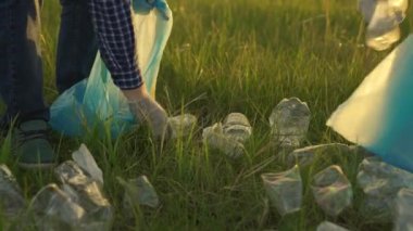 İnsanlar çimlerin üzerindeki parktaki plastik çöpleri temizlemekle meşgul. Bir işçi el, çimlerden alugaya plastik bir şişe kaldırır. Çevre dostu gezegen. Doğanın insan kirliliği