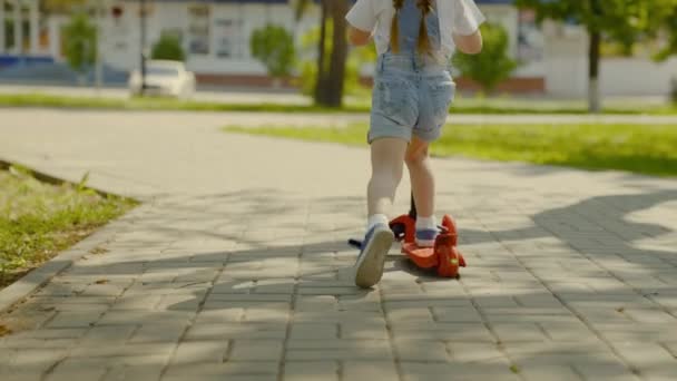 Sağlıklı bir çocuk şehirde scooter kullanıyor. Mutlu çocuk parkta oynuyor. Küçük bir kız scooter sürmeyi öğreniyor. Aile hafta sonu dışarıda. Mutlu bir çocukluk, aile, sağlık kavramı.. — Stok video
