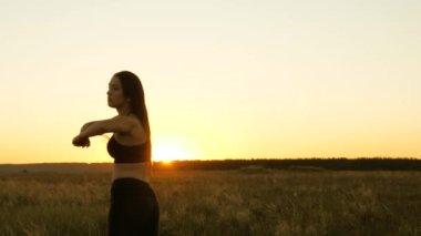 Sağlıklı, güzel bir kız şehrin dışında güneşlenir. Egzersiz ve temiz havada ısınma. Özgür genç bir kadın gün batımında yaz parkında spor yapmaya gider. Kız jimnastik yapıyor.