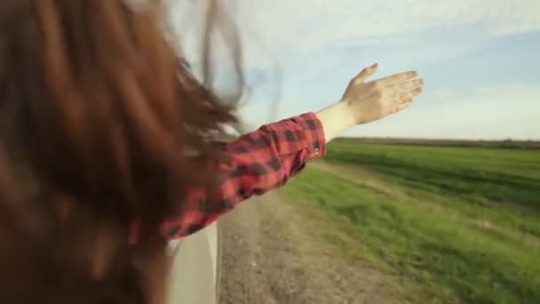 Dziewczyna podróżnik z długimi włosami podróżuje, siedzi na przednim siedzeniu samochodu, wyciąga rękę z okna i łapie blask słońca. Wolna kobieta jeździ samochodem, łapie wiatr ręką z okna samochodu. — Wideo stockowe