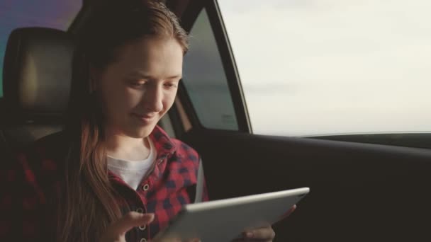 Estudiante, trabaja remotamente. Hermosa chica pasajero viaja en coche con la tableta del ordenador, sentado en el asiento trasero del coche y mira por la ventana abierta. Mujer libre está disfrutando de paseo en coche y descanso — Vídeos de Stock