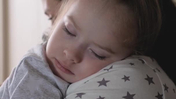 Bebé, el niño duerme en los brazos de su madre. Una joven madre cariñosa abraza a su adorable dulce hija, que se duerme en sus brazos. Amable, madre cariñosa y linda niña pequeña abrazándose en el dormitorio. — Vídeo de stock