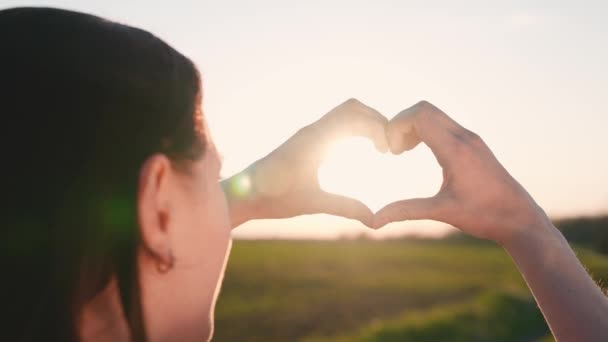 Mädchen machte Liebesherz aus ihren Handflächen. Junge Frau genießt den Sommer, entspannt. Sorglos kauendes Mädchen, das mit seinen Fingern Herzformen herstellt. Licht der sommerlichen Frühlingssonne auf Händen. Reisen und entspannen in der Natur — Stockvideo