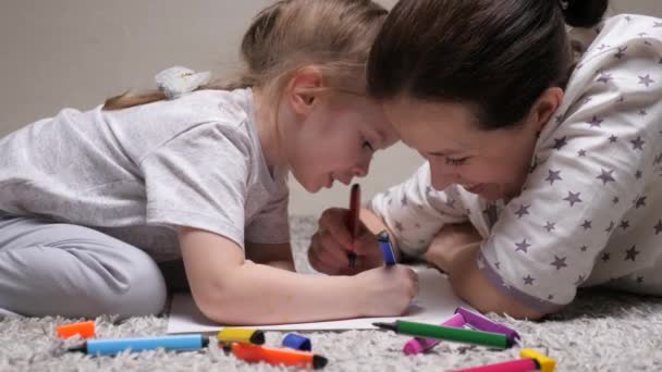 Çocuk ve anne, dadı, kıza resim yapmayı öğretiyor. Mutlu aile evde birlikte gülerek oynuyor. Bir anne kızına kağıt üzerinde resim yapmayı öğrenmesine yardım eder. Renkli kalemler ve keçeli kalemlerle boyama yapar.. — Stok video