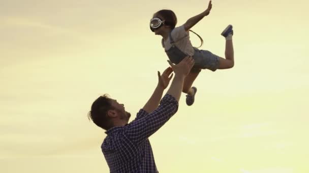 Silhouette di padre e figlio, bambine, giocare, godersi il tramonto nel parco nella natura nella giornata estiva. Famiglia felice, papà gioca con il bambino come pilota, gettandolo in cielo, bambino gioisce e ride. — Video Stock