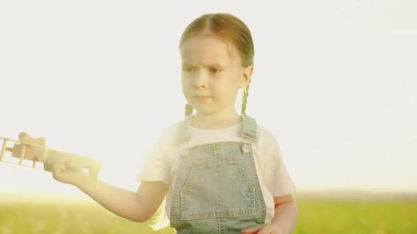 Il ragazzo tiene in mano un aeroplano giocattolo. Bambino felice, ragazza che gioca con aeroplano giocattolo sul campo estivo.Famiglia felice sta giocando nel parco. Little Daughter sogna di volare. Bambino spensierato che gioca all'aperto — Video Stock