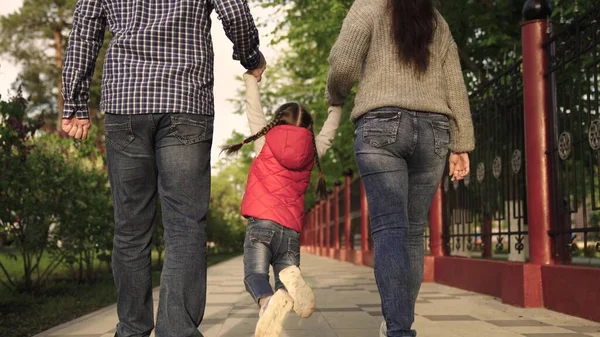 Papá, hija, mamá, están jugando en el parque de la ciudad, el niño feliz está cogido de la mano de los padres y saltando. Trabajo en equipo. La familia feliz corre en el parque en la calle, tomados de la mano en primavera, verano. Feliz infancia sana — Foto de Stock