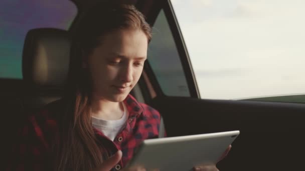 Mooie meisje passagier reist met de auto met computer tablet, zitten op de achterbank van de auto en kijkt uit open raam. Vrije vrouw geniet van autoritten en rusten. Meisje student studies, werkt op afstand — Stockvideo