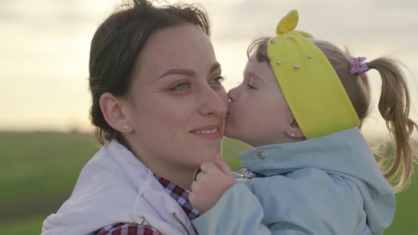 Mãe bonita, sua filhinha está abraçando no parque na primavera, verão. A mãe e o filho brincam juntos no parque infantil. O miúdo adora beijar a mamã. Mãe de família feliz, filhas sorrindo ao ar livre — Vídeo de Stock