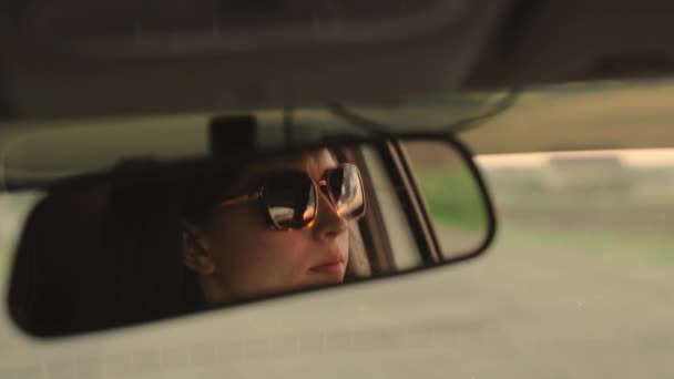 Conductora joven en gafas de sol en espejo retrovisor reflejo. Mujer joven libre viajando en coche. La conductora está conduciendo su auto. Fin de semana, coche, aventura, carretera y deportes. Taxi. — Vídeo de stock