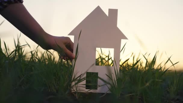 Childrens project of house in nature. Sale and insurance of real estate. Happy family construction home concept. A man, child, holding paper house in his hand on grass under blue sky, at sunset — Stock Video