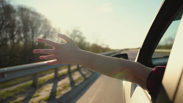 Свободная женщина водит машину и ловит ветер рукой из окна машины. Молодая девушка садится на переднее сиденье автомобиля, протягивает руку к окну и ловит сияние заходящего солнца. Концепция путешествия