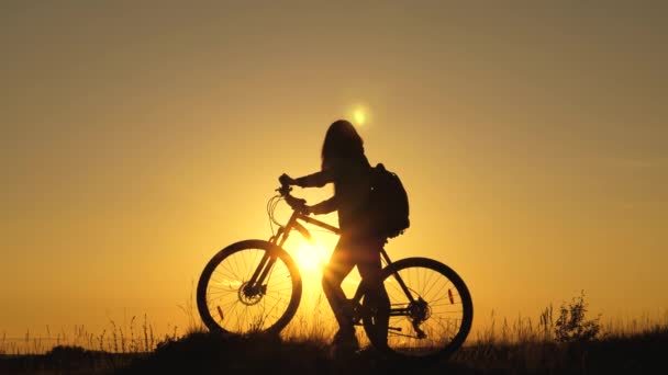 Ung kvinna turist promenader på en cykel, njuta av naturen, frisk luft i sommarparken. En fri flicka reser på cykel, vilar, tittar på solnedgången och njuter av solen. Äventyrs- och resekoncept. — Stockvideo