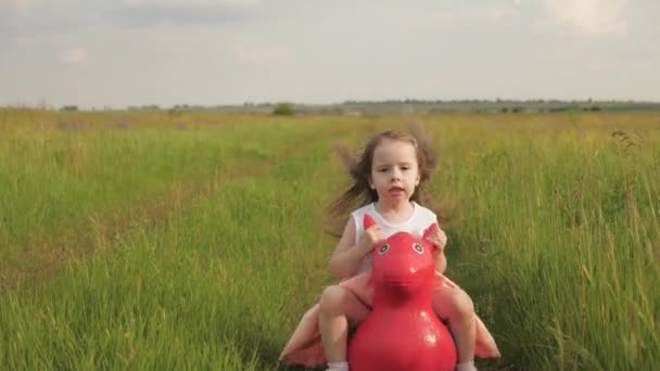 Fetiţă, fiică, jucându-se în aer liber. Familie şi copilărie, vacanţe. Fetița fericită se joacă în parc, sărind pe un cal gonflabil de jucărie. Copilul joacă pe terenul de joacă vara în natură . — Videoclip de stoc