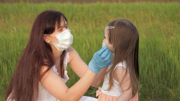 마스크를 쓰고 장갑을 끼고 있는 한 어머니는 코로나 바이러스가 유행하는 동안 여름에 거리에서 의료용 마스크를 쓰는 법을 자녀에게 가르쳐 줍니다. 어머니, 딸은 밖에서 보호용 마스크를 쓰고 있어요. 행복 한 가족 엄마, 딸 — 스톡 사진