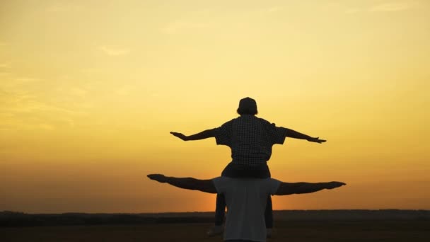 Happy dad, child playing together outdoors in front of sky. Kid dreams of flying with his dad. Family is resting in park in sun in nature. Son sits on his fathers neck, plays pilot, flies as superhero — Stock Video