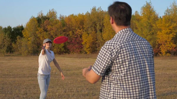 Ein Mann und eine Frau spielen und werfen sich im Park fliegende rote Scheiben zu. Unbekümmertes Paar, junge Leute, die zusammen Spaß haben. Sport und Jugend. Glückliche Familie spielt im Park, Tochter und Vater — Stockfoto