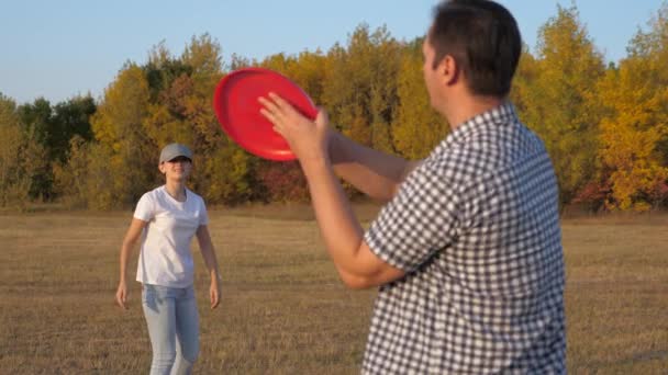A man and a woman are playing, throwing flying red disc to each other in park. Carefree couple, young people having fun together. Sports and youth. Happy family playing in park, daughter and father — Stock Video