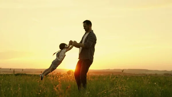 Gelukkige familie, vader speelt met kind als piloot, cirkelt kind door handen, kind verheugt zich en lacht. Silhouet van vader en kind, kleine meisjes, spelen, genieten van zonsondergang in het park in de natuur op zomerdag. — Stockfoto