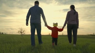 Anne, baba ve kızı sahada oynuyorlar, çocuk ebeveynlerini elleriyle tutuyor. Mutlu aile yazın gün batımında el ele tutuşarak parkta yürür. Takım çalışması. Mutlu çocukluk, aile eğitimi