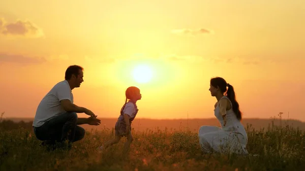 Glad familj promenader i parken vid solnedgången. Mamma, pappa och barn. Lilla dottern går från mamma till pappa, kramar och kysser sina föräldrar i solens strålar. Hälsosam familj leker ute på fältet. Lyckligt familjebegrepp — Stockfoto