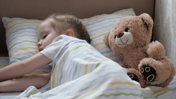 Милый малыш отдыхает в детской в своей постели. Счастливый малыш спит в кроватке со своей любимой игрушкой плюшевого мишки. Мам, папа уложил ее уставшую дочь спать. Счастливая семья и детство. Здоровые дети. — стоковое видео