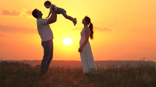 Happy family plays in summer park at sunset. Dad throws his beloved daughter up, happy child laughs and rejoices, hugs dad outdoor. Child, father, mom. Father and daughter play, dreams of flying