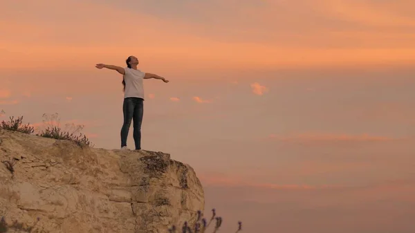 Menina caminhante relaxa e meditar no topo da colina. Jovem mulher feliz levanta as mãos, em pé no topo de uma montanha acima do mar contra o pano de fundo do céu azul. Observando o pôr do sol com uma bela paisagem. — Fotografia de Stock