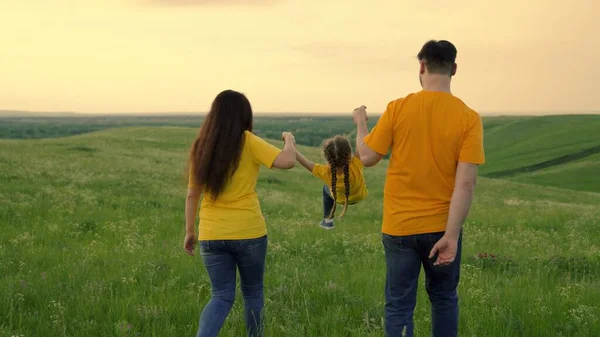 Mama, Papa und Tochter spielen auf grünem Gras auf dem Feld, ein glückliches Kind hält die Hände der Eltern und springt. Glückliche Familienläufe im Park, Händchen haltend im Frühling, Sommer. Teamwork. Familienwochenende — Stockfoto