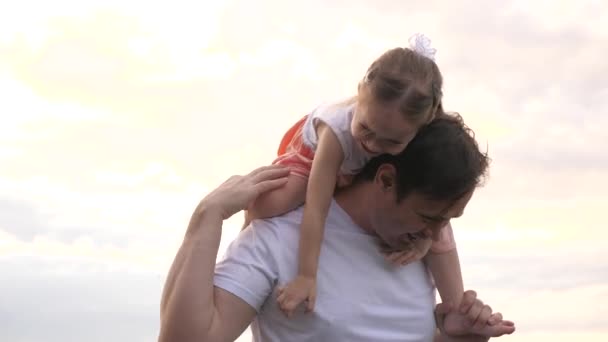 Папа и дочь веселятся вместе на свежем воздухе, ребенок, папа смеются, радуются вместе. Отец носит на плечах своего любимого ребенка перед небом. Папа и ребенок счастливы. Семья отдыхает в парке — стоковое видео