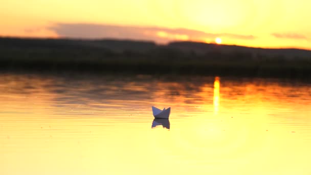 Biały papier łódź pływa w wodzie w promieniach pięknego słońca o zachodzie słońca. Statek Origami. Gry dla dzieci, marzenia o podróżach i odkryciach. Wiarygodna koncepcja przedsiębiorstwa — Wideo stockowe