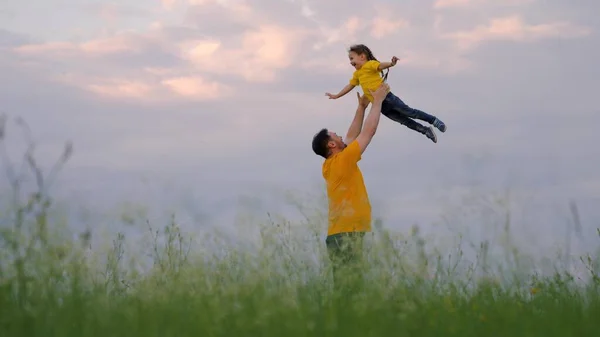 Tata rzuca swoją szczęśliwą córkę w błękitne niebo w letnim parku. Ojciec i małe dziecko bawią się, śmieją się i przytulają. Szczęśliwej podróży rodzinnej. Dziecko w ramionach rodzica. Dzień wolny od taty. Szczęśliwa rodzina — Zdjęcie stockowe