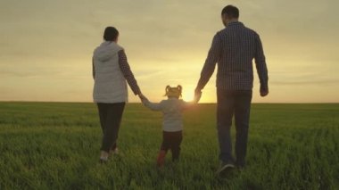 Anne, baba ve kızı sahada oynuyorlar, çocuk ebeveynlerini elleriyle tutuyor. Mutlu aile yazın gün batımında el ele tutuşarak parkta yürür. Takım çalışması. Mutlu çocukluk, aile eğitimi