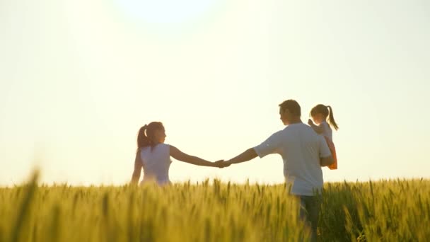 Gelukkige familie van boeren met kind, lopen op een tarweveld. Langzame beweging. Mam, pap en kind lopen hand in hand. Gezond moeder, vader en dochtertje samen genieten van de natuur, buiten. — Stockvideo