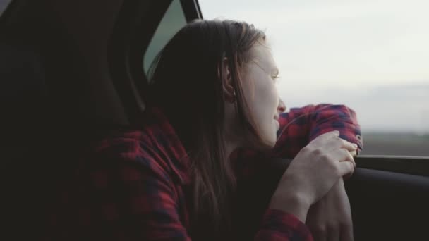 Wolna kobieta podróżuje samochodem chwyta wiatr ręką z okna samochodu. Dziewczyna z długimi włosami siedzi na przednim siedzeniu samochodu, wyciągając rękę przez okno i chwytając blask zachodzącego słońca — Wideo stockowe