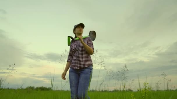 Agricultural business, agriculture. Farmer woman with shovel in her hands goes through field from work. Worker with a shovel. An agronomist walks through plantation at sunset. Growing vegetables — Stockvideo