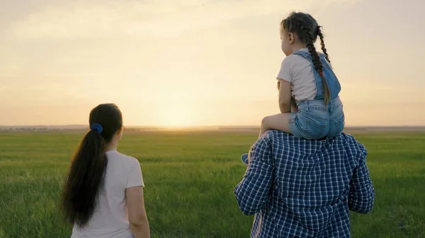 Mom, dad and daughter are playing on the field, the child is sitting on dads shoulders. Teamwork. Happy family walks in the park holding hands in the summer at sunset. Happy healthy childhood — Foto Stock