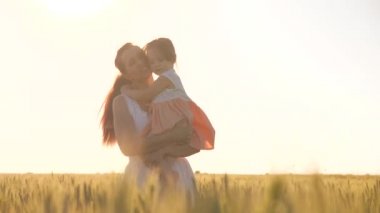 Bebek annesinin kollarında. Anne ve küçük kızı yeşil buğday tarlasında yürüyor, sarılıyor ve öpüşüyorlar. Bir çocuk ve anne buğday tarlasında yürüyorlar. İyi yolculuklar. Çiftçi kadın ve çocuk tarlada