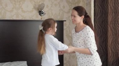 Genç anne neşeli bir şekilde gülüyor, güzel kızıyla aktif bir oyun oynuyor, çocuğu yatak odasında. Aile dansı. Mutlu aile çocuğu, kızı, anne dadısı, el ele tutuşmak, yatağa atlamak. Aile eğitimi