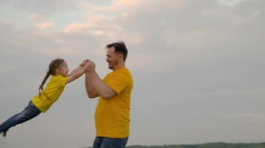 Babam oynar, mutlu kızının etrafında döner, yaz parkında gökyüzünün önünde elleri ile. Baba ve küçük çocuk birlikte sevinir, güler ve sarılırlar. İyi yolculuklar. Bebek ebeveynlerin kollarında. Mutlu aile