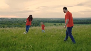 Mutlu aile, kız, baba, anne yazın parkta birlikte futbol oynuyorlar, yeşil çimlerde, birbirlerine pas veriyorlar. Anne, baba ve çocuk hafta sonları doğada aktif bir oyun oynarken eğleniyorlar.