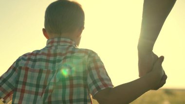 Baba ve oğul güneşin altında parkta el ele yürürler. Parktaki insanlar. Mutlu aile yürüyüşçüsü ve babası dışarıda. Mutlu aile çocukluk hayali kavramı. Ebeveynler ve neşeli çocuklar. Oğlu ve babası birlikte.