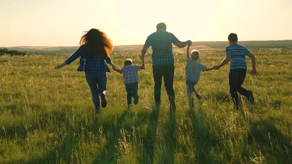 Glad familj team, springa tillsammans hålla händerna i parken. Lyckliga söner, barn, mamma och pappa springer, leker, gläds, njuter av naturen på sommaren. Lagarbete av människor. En grupp människor i olika åldrar vid solnedgången. — Stockfoto