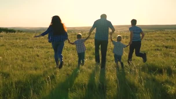 Szczęśliwa rodzinna drużyna, trzymająca się za ręce w parku. Szczęśliwi synowie, dzieci, mama i tata biegają, bawią się, radują się, cieszą się przyrodą latem. Praca zespołowa ludzi. Grupa ludzi w różnym wieku o zachodzie słońca. — Wideo stockowe